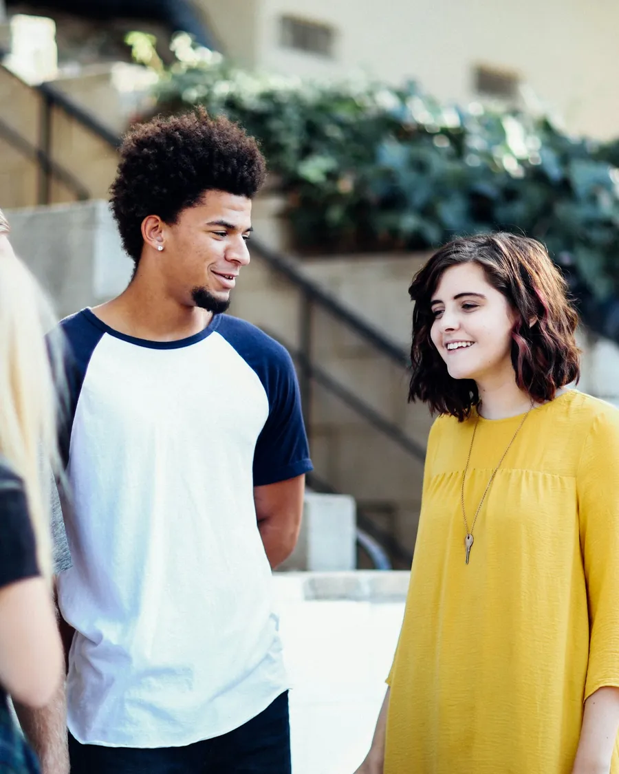 Three students talk outside a building, one laughing.