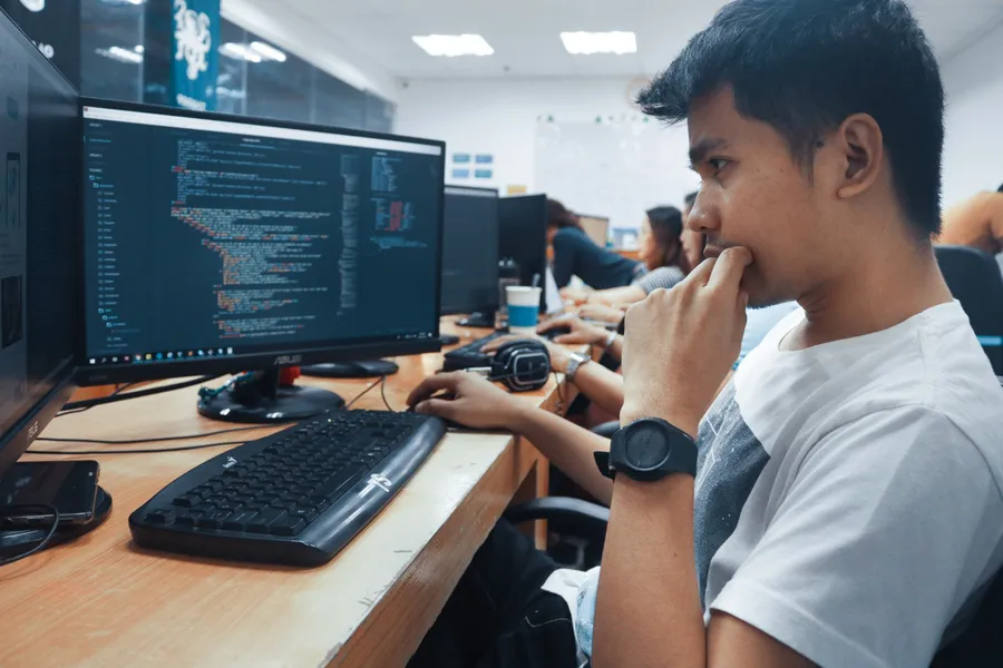 A student sits at a computer with code on the screen in a busy lab.