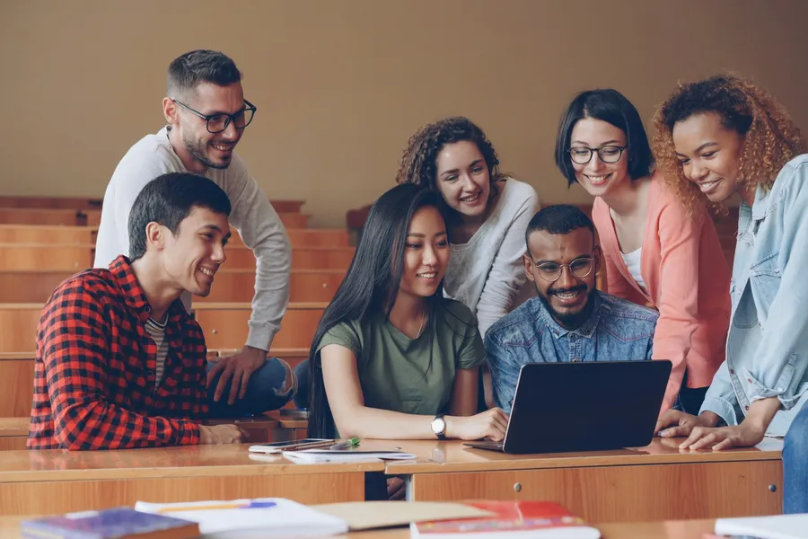 A group of students smile and wave at a laptop screen.