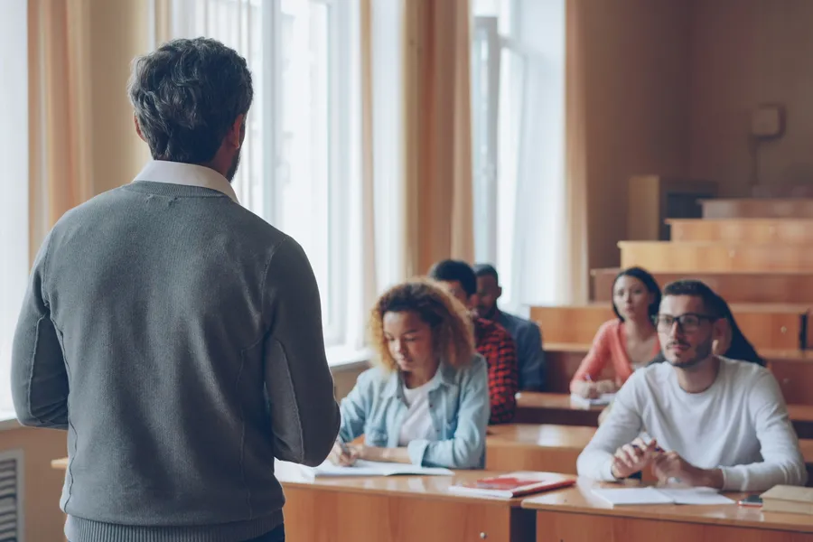 A professor stands at the front of a classroom while students take notes.