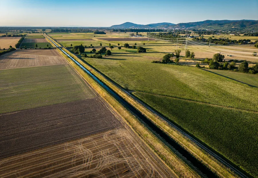 Aerial view of a long canal running between farm fields toward distant hills.