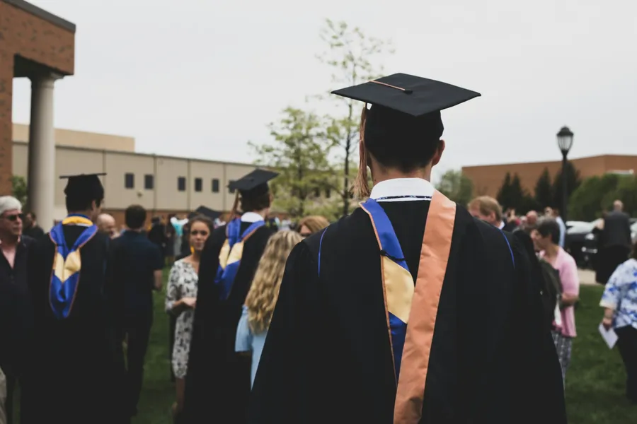 A graduate in cap, gown and stole stands among families after a ceremony.